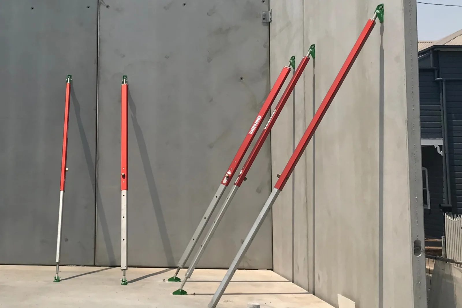 Adjustable alumunium tilt props are installed against a concrete wall, anchored at the base and fixed at the top for structural support.