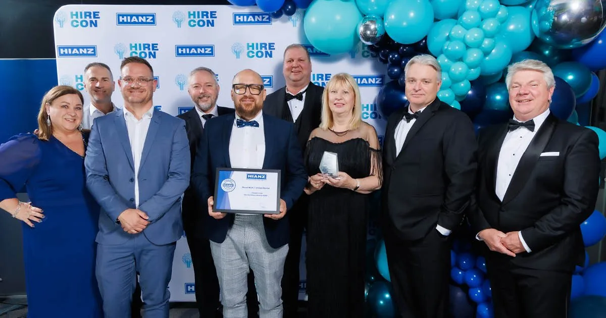 Employees smiling and holding awards, standing in front of a company logo backdrop at a recognition event.