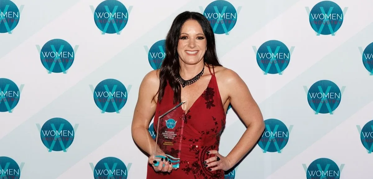 Smiling employee holding an award in front of a company-branded backdrop, recognized for excellence in site safety and barrier services.