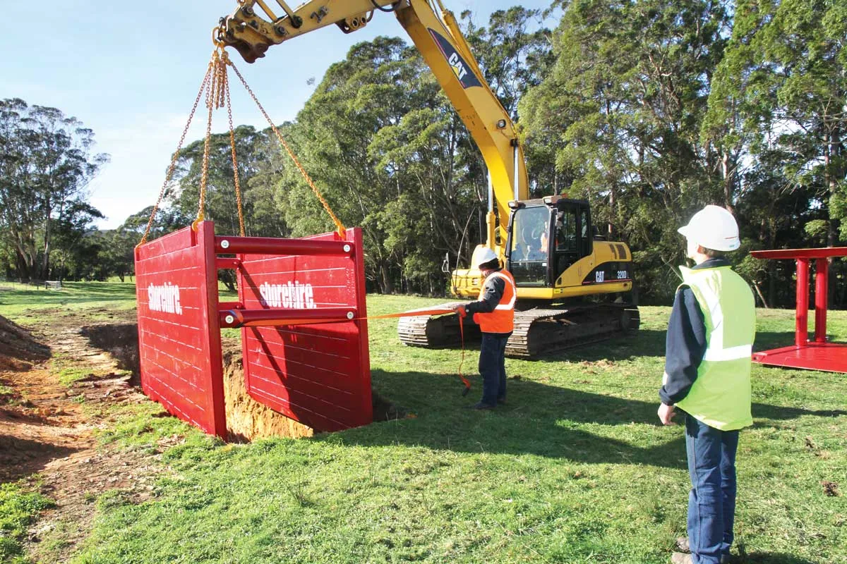 Workers lowering a protective box into an excavation site to ensure trench safety during construction work.