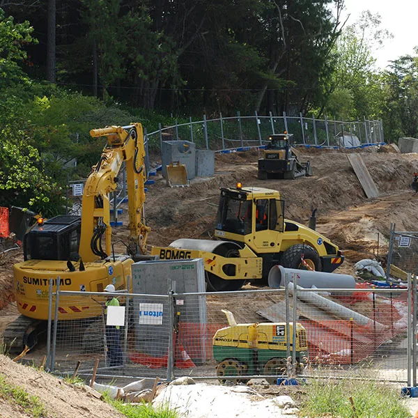 Different types of construction equipment in use at a site, supporting tasks like excavation, lifting, and barrier installation.