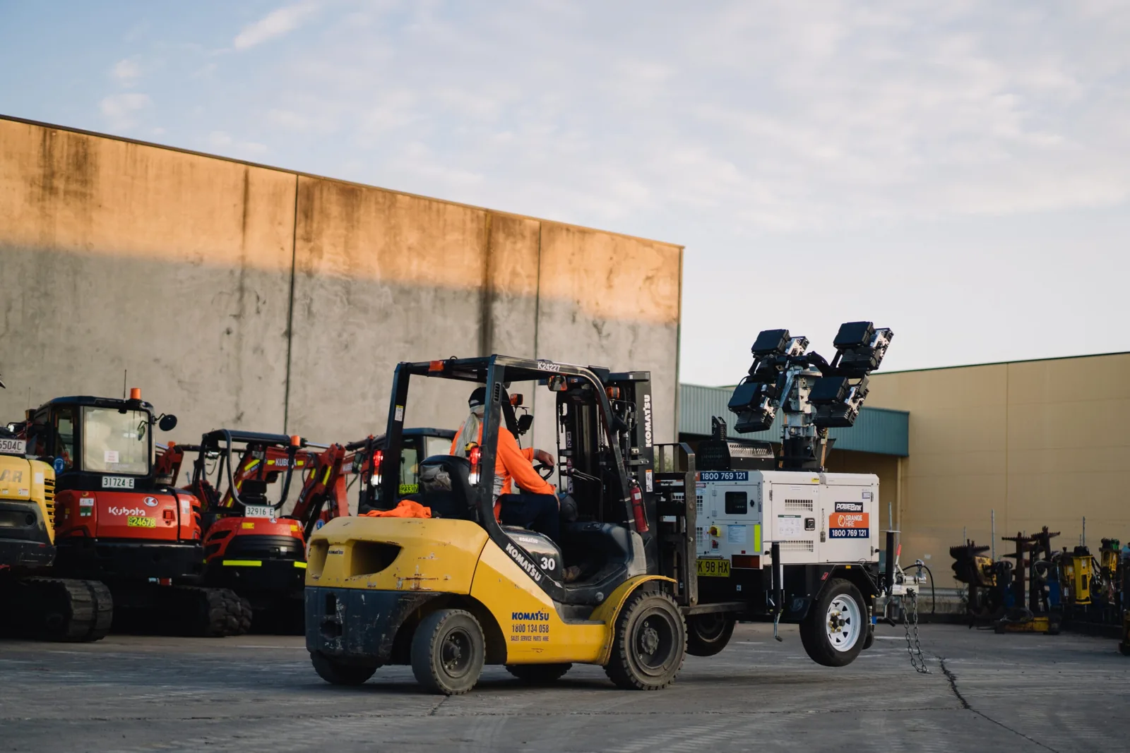 A man driving a truck equipped with a mounted plate compactor on top, used for compacting soil at a construction site.