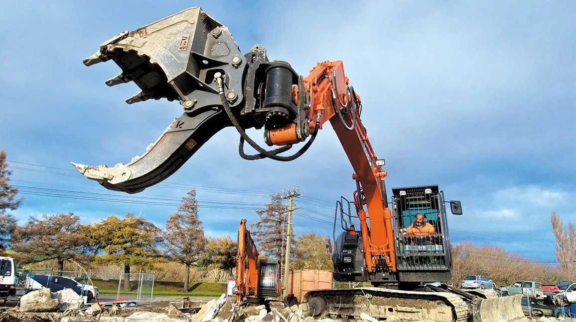 A man operating an excavator at a construction site with safety barriers installed around the work area.
