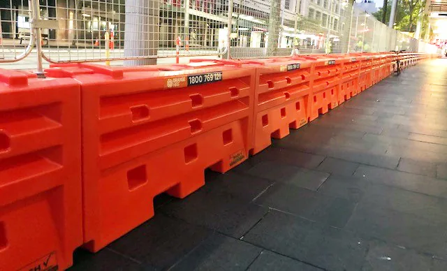 Long row of water-filled safety barriers lined up along a road construction site to protect workers and guide traffic.