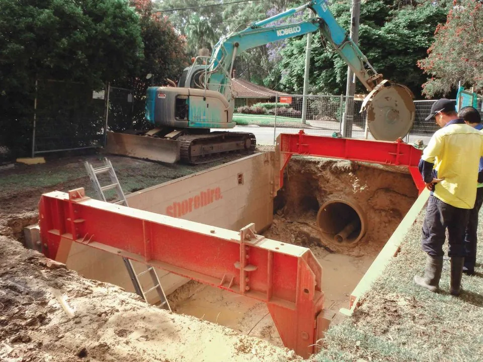 Worker examining an underground excavation site containing various construction materials for stability and safety assessment.