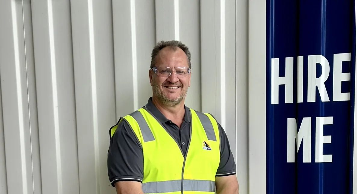 Man standing and smiling confidently in an outdoor setting, conveying positivity and professional presence.