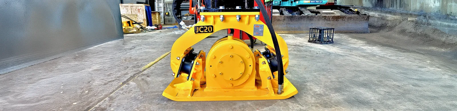 Plate compactor machine on a construction site near safety barriers, used for compacting soil and maintaining ground stability.
