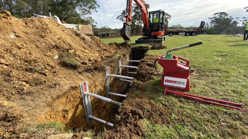 Construction site with a small panel placed inside a digging hole, surrounded by safety barriers and warning signs.