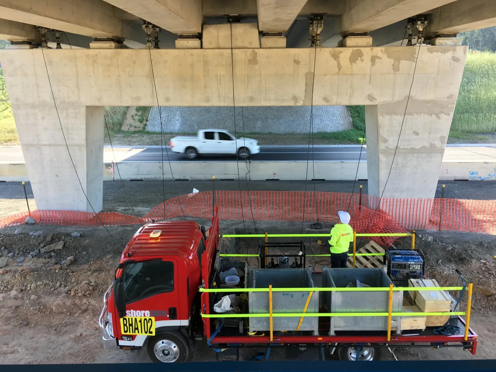 Worker on truck under bridge guiding ropes lifting structure with hydraulic jack during construction setup.